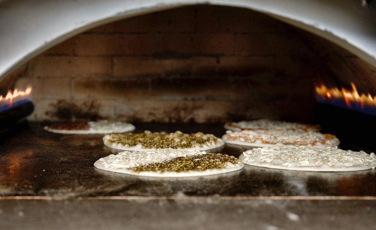 Cheese and zaatar manakish baking on the stone floor of the oven at Sahtein Bakery