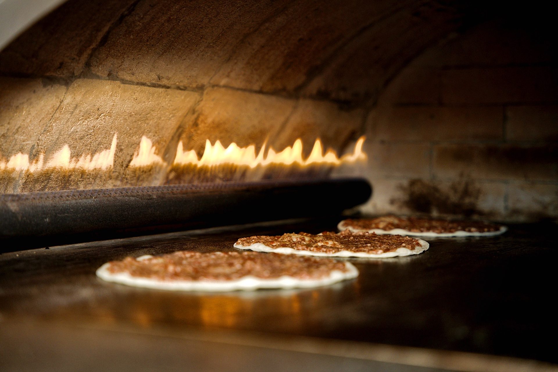 Lahm baajin baking beside the open flame inside the Sahtein Bakery stone oven