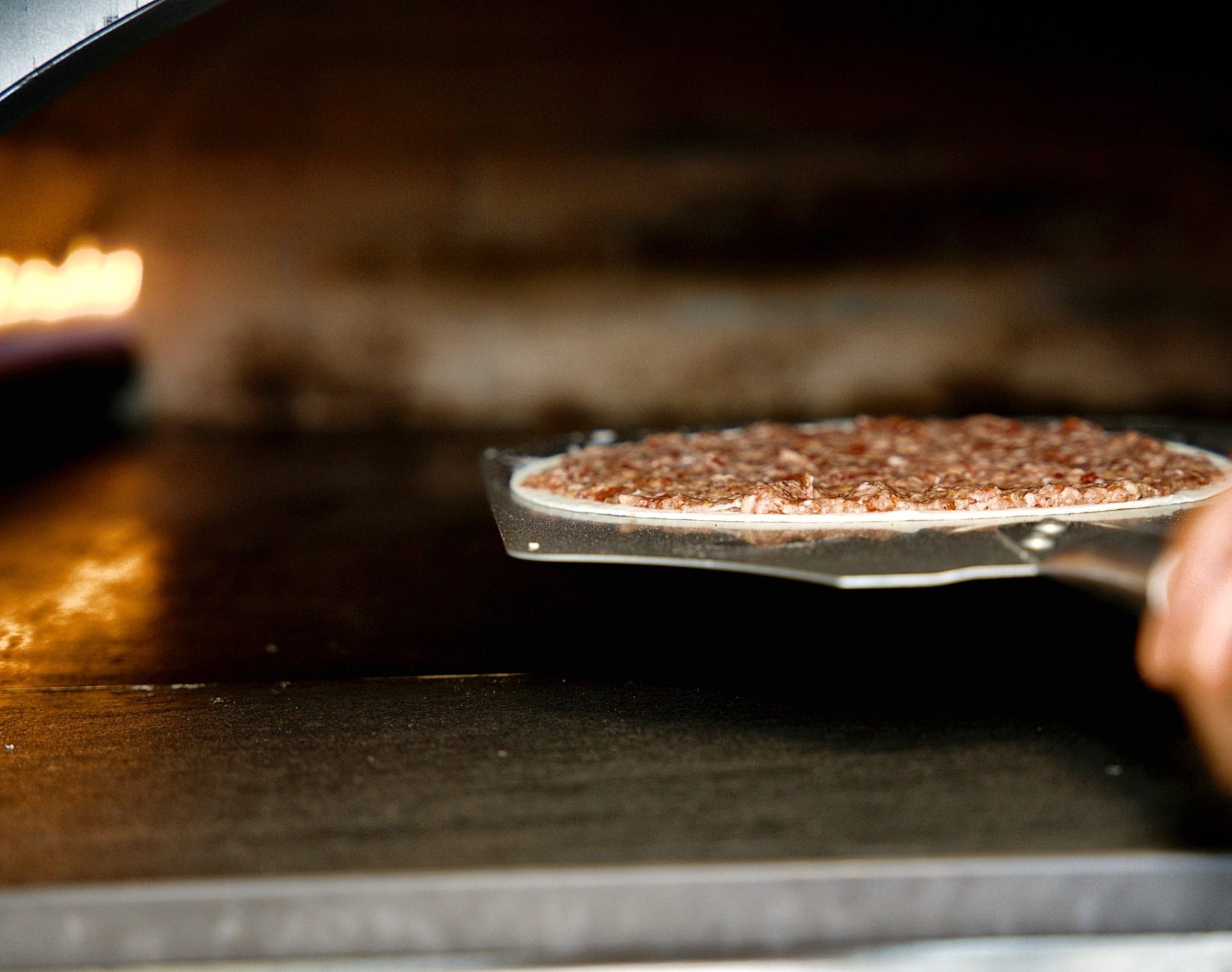 A baker sliding a fresh lahm baajin into the hot oven on a metal peel