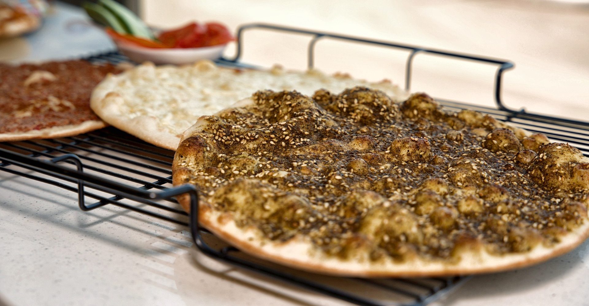 Zaatar manakish resting on a cooling rack beside cheese and meat manakish