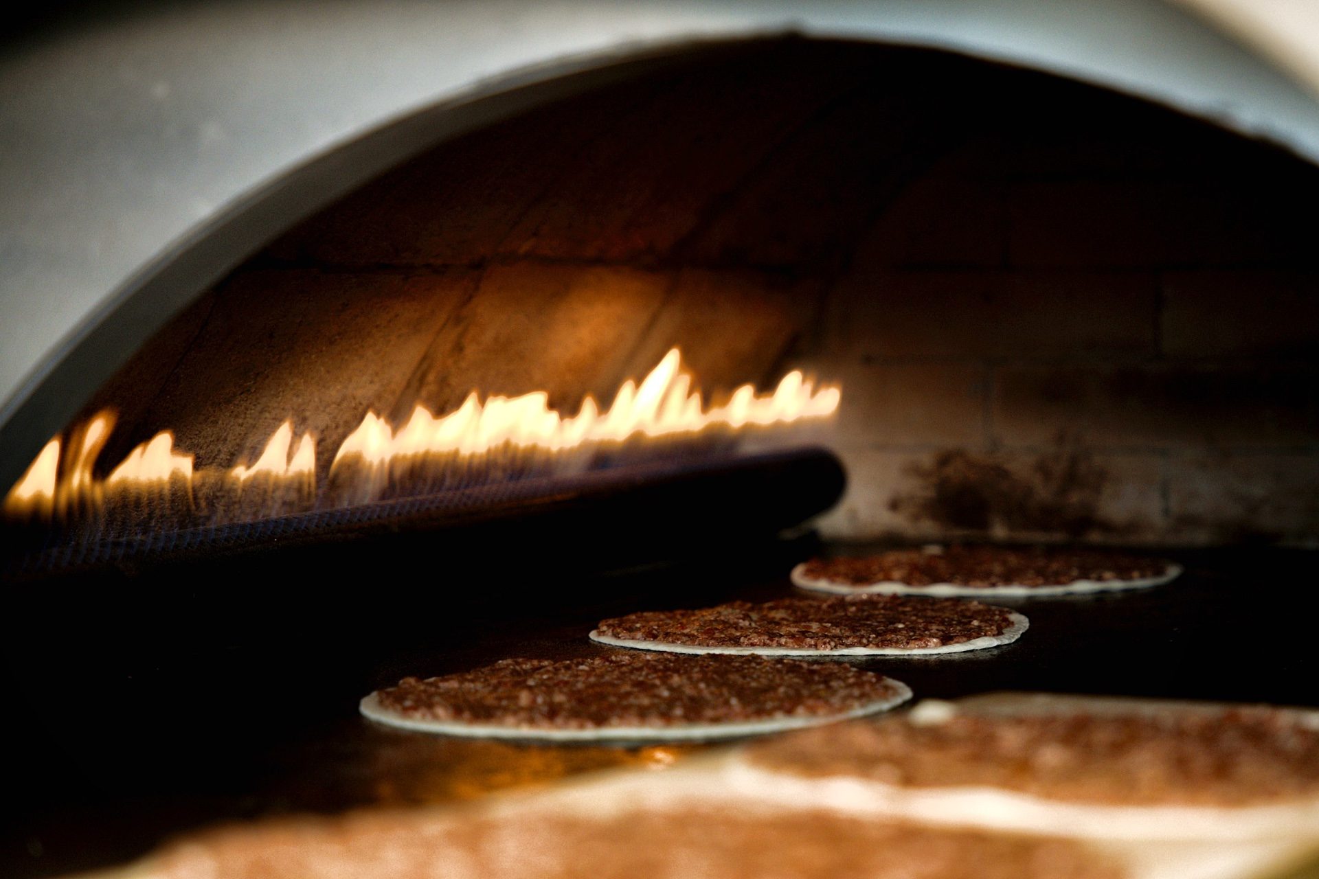 Rows of lahm baajin cooking under the roaring flame of the stone oven